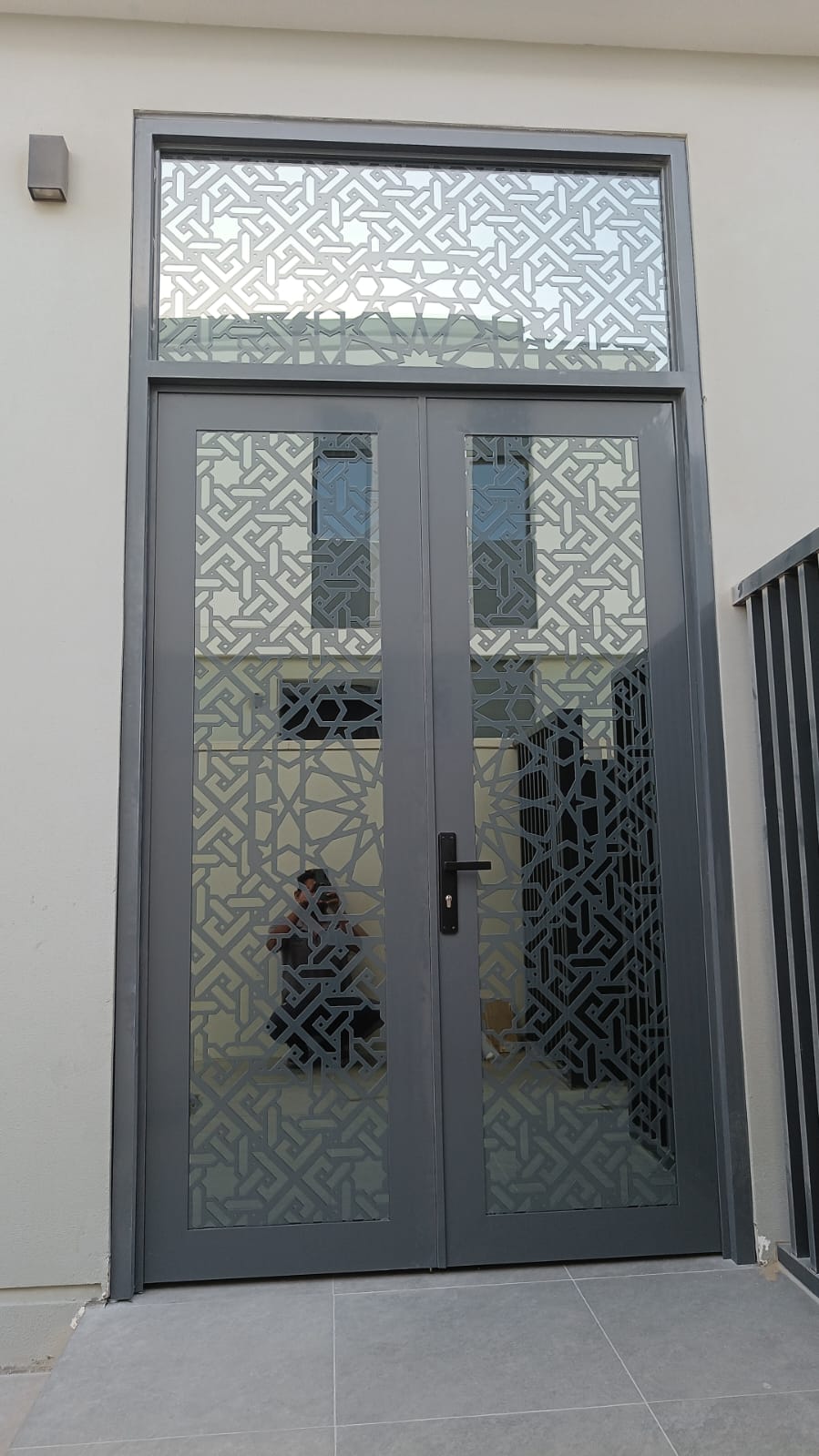Modern dark metal pergola with slatted roof on a large light grey tiled patio of a contemporary home